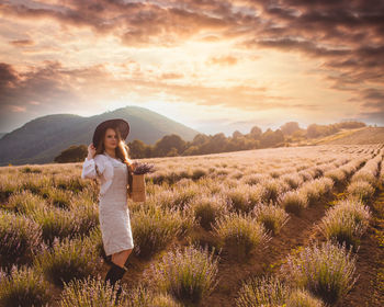 Woman standing on field against sky during sunset