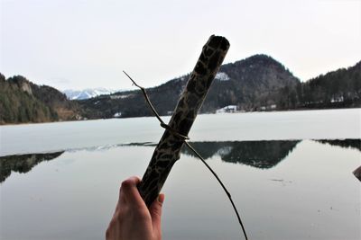 Close-up of hand holding water in lake against sky