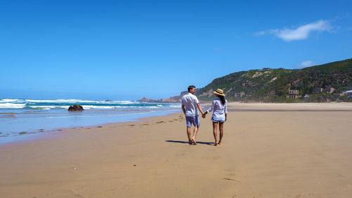 Rear view of woman walking at beach against blue sky