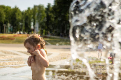 Shirtless girl by spraying water fountain at park