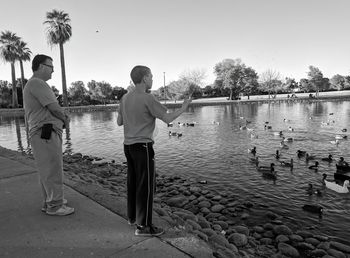 Rear view of people standing by lake against clear sky