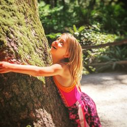 Cute girl holding tree trunk at park