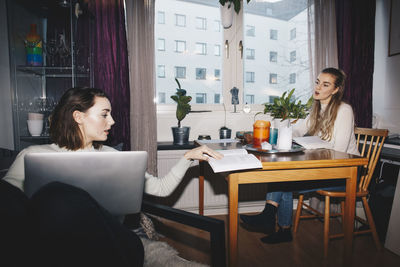 Young female students discussing book in college dorm room