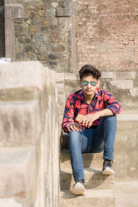 Portrait of young man sitting against wall