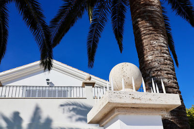 Low angle view of house and palm trees against blue sky