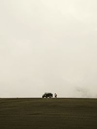 Distant view of woman standing by car on field against sky