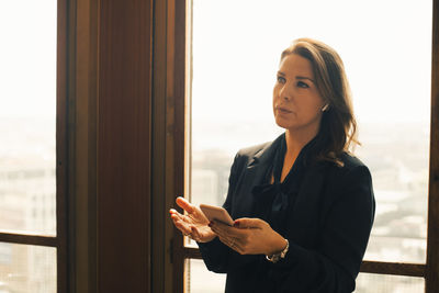 Thoughtful female mid adult lawyer talking on smart phone through bluetooth at office