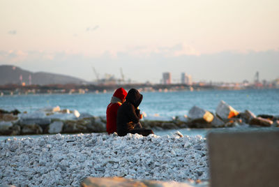 Rear view of girl sitting on retaining wall against cloudy sky