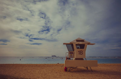 Scenic view of lifeguard hut on beach against cloudy sky