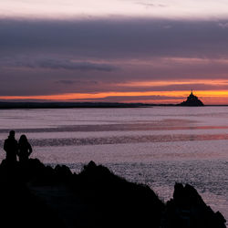 Silhouette rocks on beach against sky during sunset