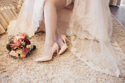 Low section of bride in wedding dress sitting on bed