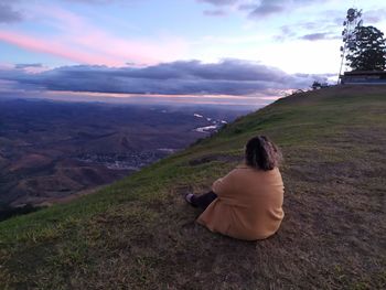 Rear view of woman sitting on landscape against sky