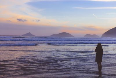 Woman standing by the sea at dusk