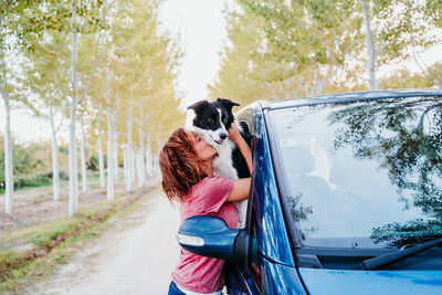 Side view of woman kissing dog through car window
