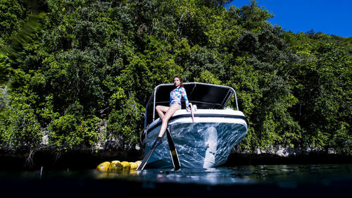 Woman sitting on boat in sea against trees