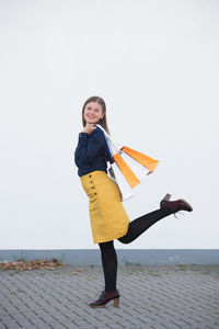 Portrait of smiling young woman standing against wall