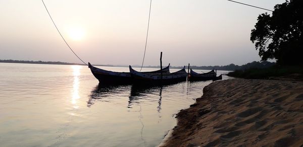 Sailboats moored on sea against sky during sunset