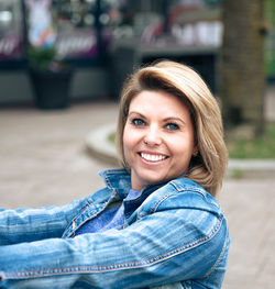 Confident woman in denim jacket smiling, embracing herself