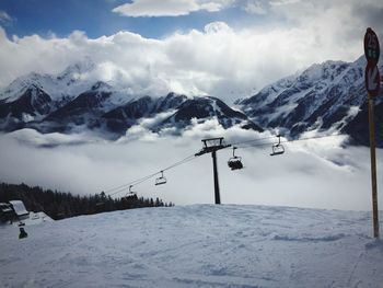 Ski lift over snowy hill against snowcapped mountains and cloudy sky