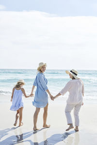 Mother, daughter and grandmother walking by the sea, rear view