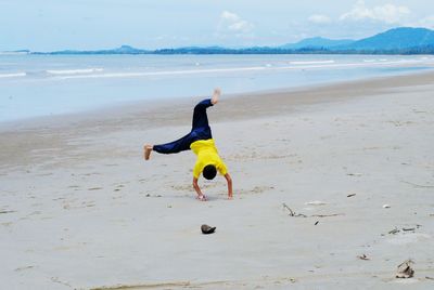 Rear view of man exercising on sand at beach