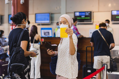Asian woman in face mask check in at airport and showing her vaccination record