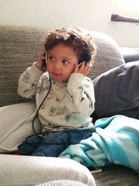 Boy wearing headphones while sitting with parent on sofa at home