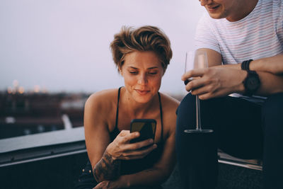 Woman using smart phone while sitting by friend having wine on terrace