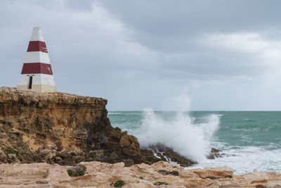 Lighthouse on rocks by sea against sky