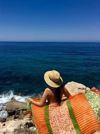 Rear view of woman sitting on beach against clear sky