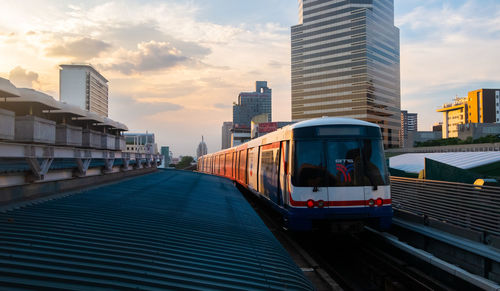 Train by buildings in city against sky during sunset