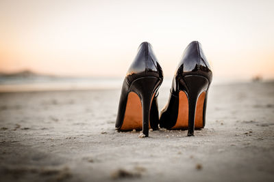 Close-up of shoes on beach against sky during sunset