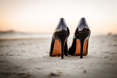 Close-up of shoes on beach against sky during sunset