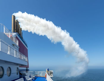 A ferry bound for england trails a dense white cloud of exhaust fumes from its funnels.