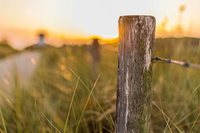 Close-up of wooden post on field against sky at sunset