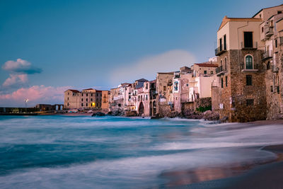 Buildings by sea against blue sky