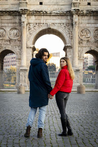 Young couple traveling to rome. young couple holds hands and strolls in front of the arch of titus.