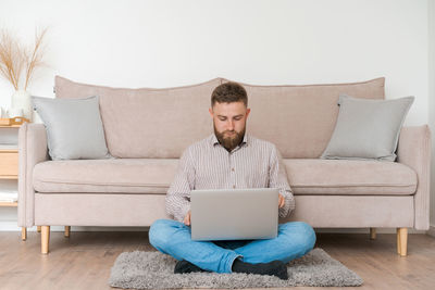 Young attractive man sitting on sofa at home, working on laptop online, using