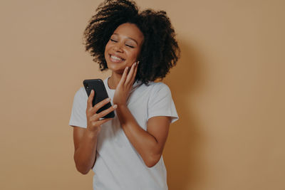 Young woman using phone while standing on wall