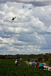 People on airplane flying over field against sky