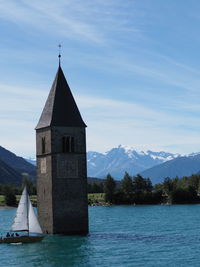 Church and boat on lago di resia - italy. church by lake and buildings against sky