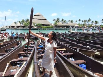 Young woman holding oar while standing in boat moored at harbor