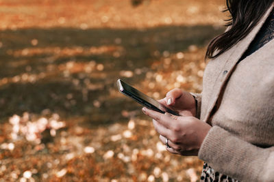 Mid section of woman using mobile phone, texting, fall, autumn.