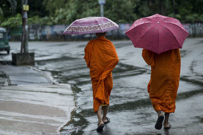 Rear view of monks with umbrellas walking on street