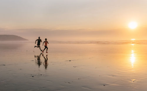 Athletes couple running on the beach at sunset