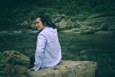 Young woman sitting on rock by river