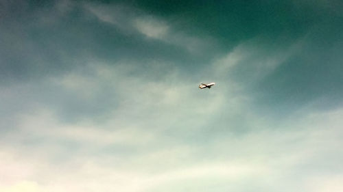 Low angle view of airplane flying against cloudy sky