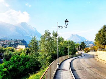 Street amidst trees and mountains against sky