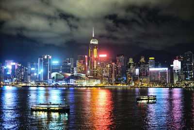 Illuminated buildings by river against sky at night