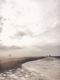 People at beach against cloudy sky